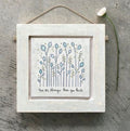 Small square East of India distressed whitewashed wooden framed picture featuring a delicate wildflower illustration with blue-grey poppy-style flower heads and small gold dot details on a white background, with the sentiment "You are stronger than you think," hung with natural jute twine.