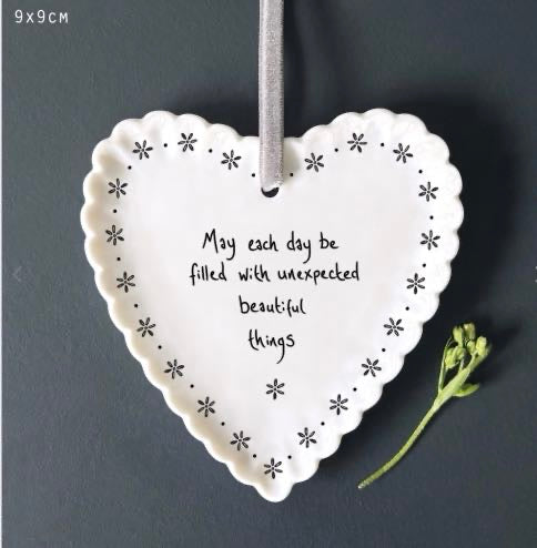 White East of India porcelain hanging heart decoration with scalloped border and black floral details, reading "May each day be filled with unexpected beautiful things," hung from a grey satin ribbon.