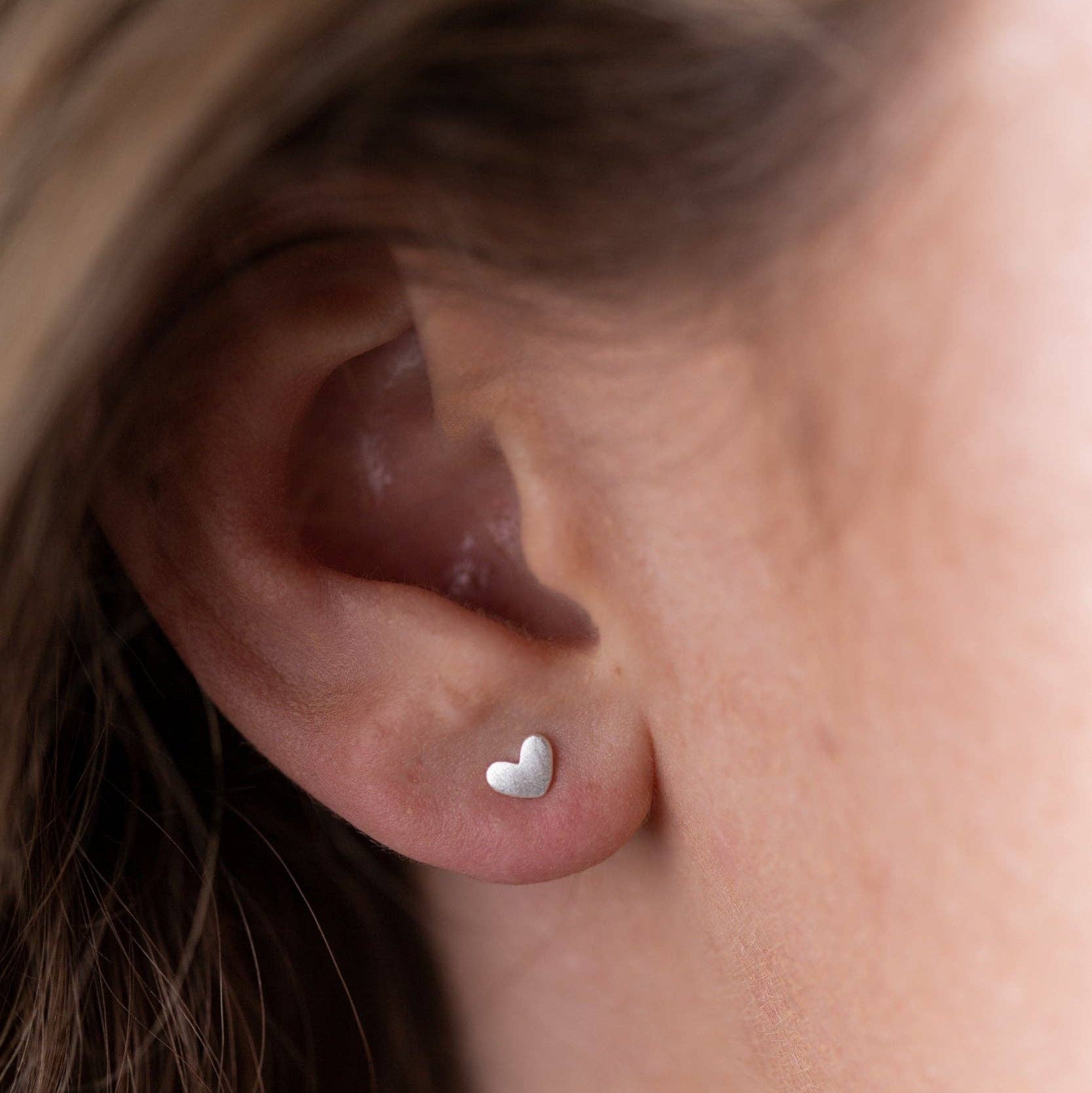 Sterling silver heart stud earrings worn in ear – minimalist heart studs